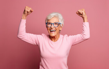 Elderly attractive woman with a happy, proud and satisfied expression on face, raising one hand with a dumbbell, showing strength of her musculs, celebrating sport achievement