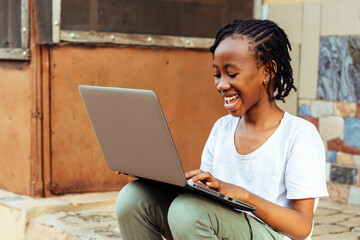 excited young African child using a laptop on the ground