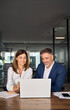 © Stock 4 You - Team of diverse partners sitting at table mature Latin business man and European business woman discussing project on laptop in office. Two colleagues of professional business people working, vertical