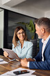 © Stock 4 You - Vertical shot of team of diverse partners mature Latin business man and European business woman discussing project at table in office. Two colleagues of professional business people working on tablet.