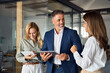 © Stock 4 You - Group of diverse partners mature Latin business man and European business women discussing project on tablet in office. Team of colleagues professionals business people working together at workspace.