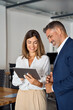 © Stock 4 You - Vertical portrait of mature Latin businessman and European businesswoman discussing project on tablet in office. Two diverse partners colleagues of confident professional businesspeople work together.