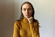 Studio portrait of pretty tired exhausted millennial caucasian female looking at camera with sad face expression, touching her chin, wearing yellow turtleneck. Student girl upset with results of exam