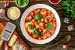 Gnocchi alla sorrentina - gnocchi with melted mozzarella cheese in tomato sauce and  Parmigiano Reggiano on wooden table
