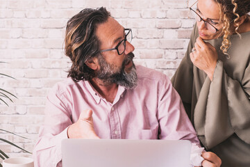 Man talking with woman at office in front of a computer. Concept of team worker couple working together on online small business. Adult people using computer and wearing glasses. Modern technology