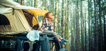 Freedom Feeling And Adventure Lifestyle People. Traveler Adult Female Chilling Outside Her Car Vehicle Roof Tent And Enjoy Nature Sounds Smiling. High Trees Forest Green Woods Background. Scenic Place