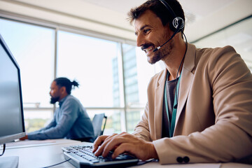 Wall Mural - Happy male entrepreneur with headset working on computer in office.