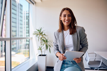 Wall Mural - Young happy businesswoman using touchpad while working in office and looking at camera.