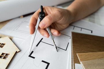 Female architect or interior designer holding compass drawing tool. Woman working on home floor plans. Building structural blueprint projects on the table. Design studio desk scene.