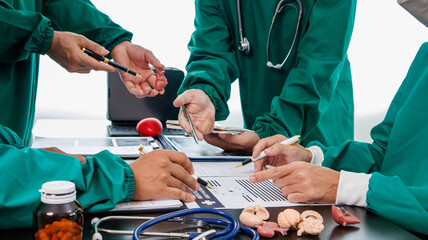 Wall Mural - Multiracial medical team having a meeting with doctors in white lab coats and surgical scrubs seated at a table discussing a patients records