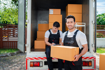 Asian Couple check while unloading boxes and furniture from a pickup truck to a new house with service cargo two men movers worker in uniform lifting boxes. concept of Home moving and delivery.