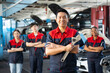 © Siam Stock - Selective focus of mid-adult Asian male mechanic in uniform, standing to hold a large adjustable spanner with arms folded and smiling at camera with a blurred mechanic team standing in the background.