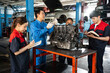 © Siam Stock - A middle-aged Asian senior male mechanic in blue uniform, standing to explain about the car engine placed on table to three junior mechanics who were listening and writing down in notebooks at garage.