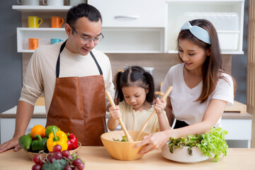 Wall Mural - Happiness asian family with father, mother and daughter preparing cooking salad vegetable food together in kitchen at home, happy dad, mom and kid cooking breakfast with salad, lifestyles concept.