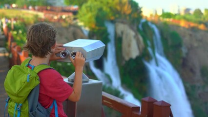 Wall Mural - A little boy is portrayed visiting the Lower Duden waterfall in the picturesque city of Antalya. He is observing the waterfall through a binoculars installed at the viewpoint