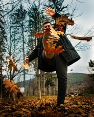 Poster - Vertical shot of a young male kicking up dry autumn leaves in a forest