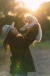 Young Caucasian woman wearing a hat standing in grassy field, lovingly holding Golden Retriever dog