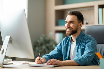 Aufkleber - Young Smiling Businessman Taking Notes While Working On Computer In Office