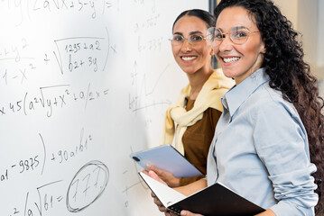 Portrait of two cute high school female Arab students having fun while solving a problem on a white board. Girls stand near the blackboard and prepare to enter the math college. Business woman in acti