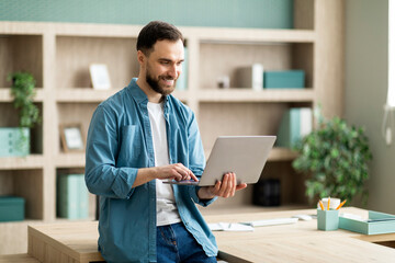 Aufkleber - Smiling Businessman Using Laptop Computer While Standing Near Desk In Modern Office