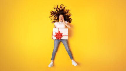 Excited Young Woman Posing With Wrapped Gift Box, Yellow Background