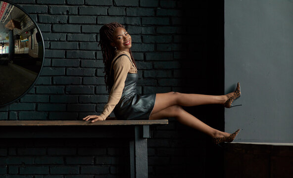 Playful black woman looking at the camera and smiling with her legs levitating wearing trendy leopard high-heeled pumps. Joyful black lady, a business manager or an employee of a startup company.