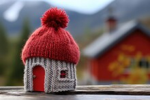 A Cute Little House Sitting On A Table With A Red Knitted Bobble Hat Resting On Top Of It, Captured In A Close Up Shot.