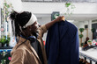 © DC Studio - African american man holding blazer in clothing store, examining fabric and size. Customer looking at formal jacket on hanger while choosing new outfit in shopping center boutique