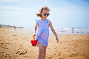 Sticker - Adorable preshooler girl playing on the sand beach at Atlantic coast of Brittany, France