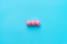 High Angle View Of Three Bright Pink Eggs Prepared For Easter Celebration Lying On Center Of Turquoise Surface 