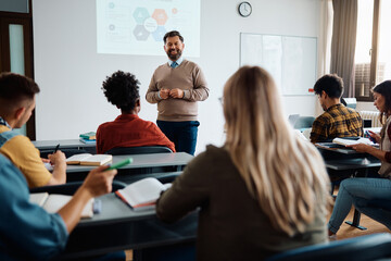 happy mature teacher talks to his students while holding presentation in lecture hall.