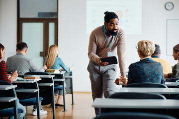 black adult education teacher talks to senior woman during course in lecture hall.