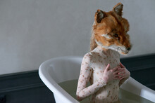 Young Woman In Wet Bodysuit And Fox Mask On Her Head Sitting Straight In Tub And Covering Breast With Her Hands As If Protecting From Outside World  