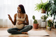 © Drobot Dean - Black pregnant woman smiling and using cellphone during yoga practice