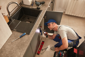 Wall Mural - Plumber fixing and repairing water pipes under the kitchen sink.