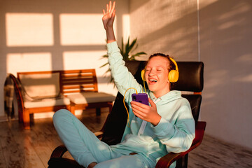 Wall Mural - Beautiful young woman in headphones sits on sofa and enjoys listening to music