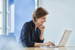 © Westend61 - Smiling businesswoman using laptop at desk in office