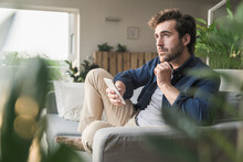 Young Man Sitting On Couch At Home, Using Smartphone