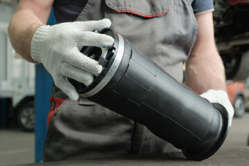 Repair of the suspension of a large SUV at a service station.Replacement of the pneumatic cylinder. An auto mechanic holds a new pneumatic cylinder in his hands, checks its integrity. 