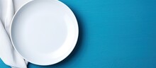 This Image Is Of An Empty White Plate And A Cotton Napkin On A Blue Background. It Is A Food Background Suitable For A Menu Or Recipe Book. The Table Setting Is Shown From A Top-down View, And Is