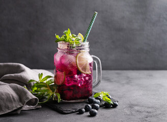 Refreshing blueberry mojito or lemonade with lime, mint and ice on a dark background. Summer healthy non-alcoholic drink made from fruits and berries.