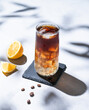 Coffee cold brew with tonic in a tall glass with ice and lemon on a light blue background with coffee beans and shadow. Trendy summer craft refreshing drink.