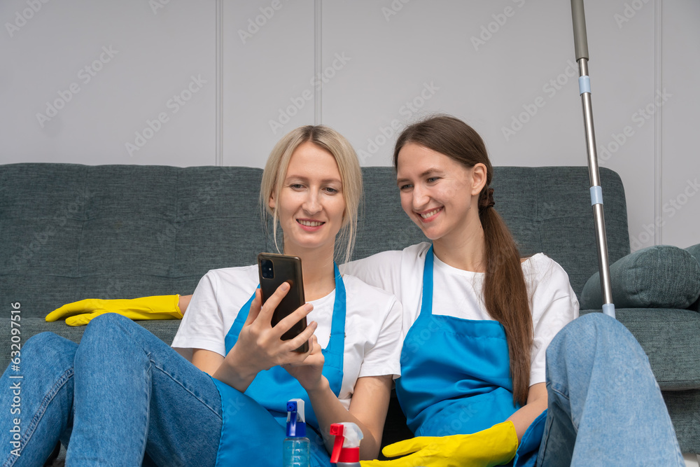 Two young beautiful women in uniforms and aprons from cleaning company ...