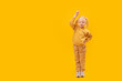 © somemeans - Smiling little girl points her finger up. Full-length portrait of preschool girl, bright yellow background. Copy space, space for text