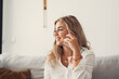 © Daniel - Happy cheerful young woman talking on the phone at home, smiling teen girl making answering call by cellphone sitting on couch, beautiful lady having pleasant funny conversation speaking by mobile.