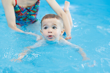 Wall Mural - A 2-year-old boy learns to swim in a pool with a coach. Swimming lessons for children. Swimming school for children. Educational swimming courses for children