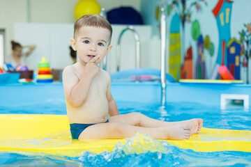 Wall Mural - Development for babies. A little boy is learning to swim in the pool. Children's first swimming lessons. Development for babies