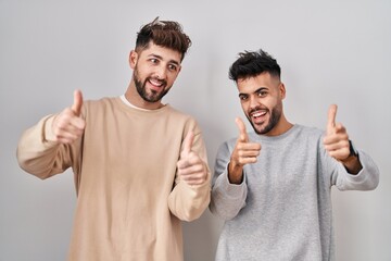 Wall Mural - Young homosexual couple standing over white background pointing fingers to camera with happy and funny face. good energy and vibes.