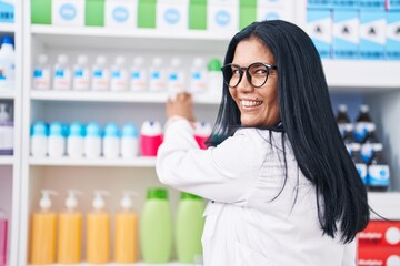 Wall Mural - Middle age hispanic woman pharmacist smiling confident holding medication on shelving at pharmacy