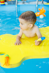 Wall Mural - Little cheerful 2-year-old boy is learning to swim in the pool. Swimming lessons for children. Swimming school for children.